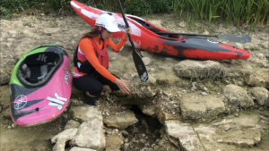 Femme à côté de kayak qui montre un trou dans la roche, dans une rivière